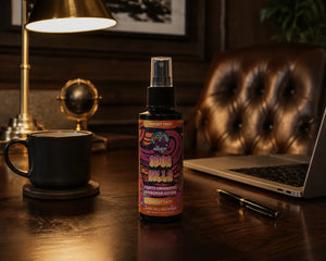 Front view of Odor Killa air freshener  in Sunset Sway sitting on a wooden desk in front of a brown leather chair in a fancy home office. 