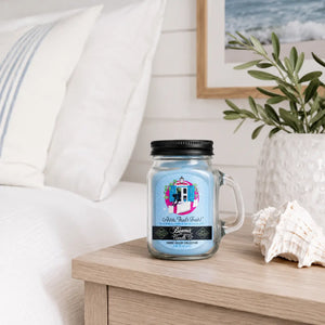 Ahh That's Fresh Beamer Co Candle sitting on light wood bedside table next to bed with crisp white linens and coastal decor