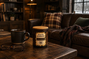 White Russian Reserve Candle sitting on  wooden coffee table in rustic style  living room with brown leather couch and flannel pillows