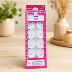 Pack of Rose t-lite candles in a pink box on a wooden surface with decorative items in the background.