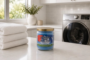 Clothesline Fresh Odor Exterminating Candle sitting on laundry room counter near washing machine and folded white towels. 
