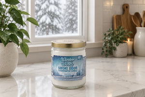Winter Winds Smoke Exterminator Candle sitting on white kitchen counter in front of window with snowy trees outside.
