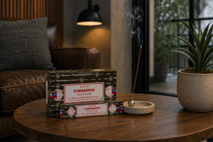Front view of Satya Cinnamon Incense sticks on a wooden table in a tidy,  masculine style living room with burning incense stick. 