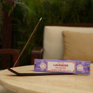 Lavender incense stick burning on a wooden table with a box of incense in the background.