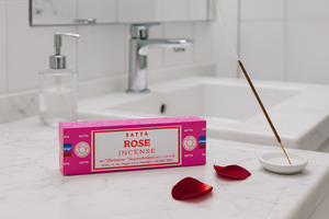 Box of Satya Rose Incense on a bathroom counter with incense stick and rose petals.